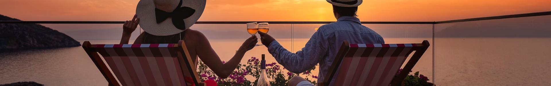 Coppia che brinda seduti su due sdraio al tramonto sul mare
