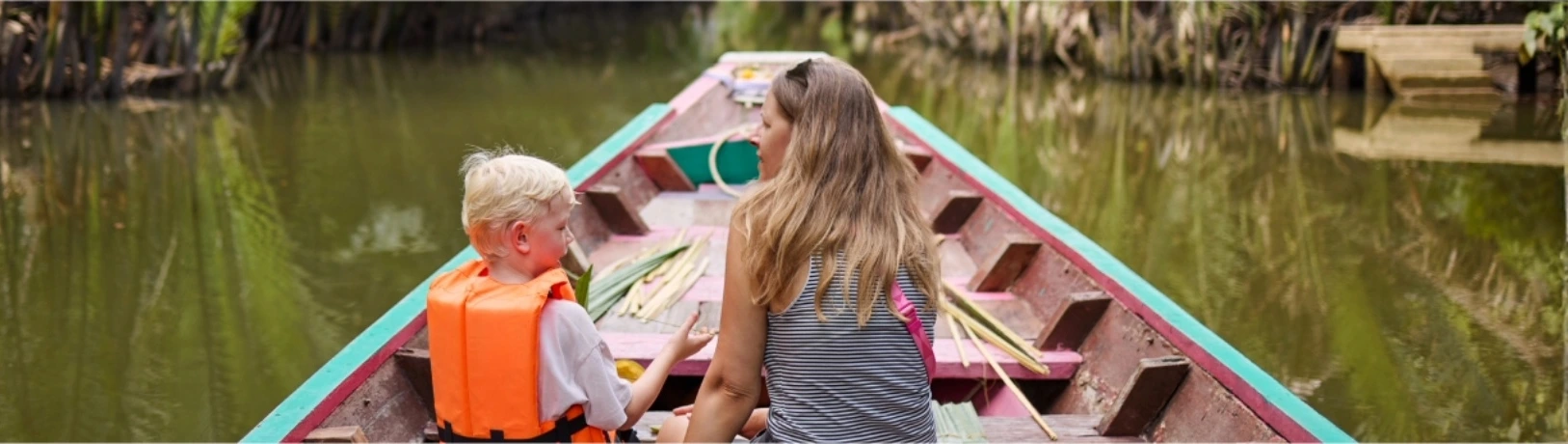 mamma e figlio seduti su una barca tradizionale che navigano in un fiume in Thailandia