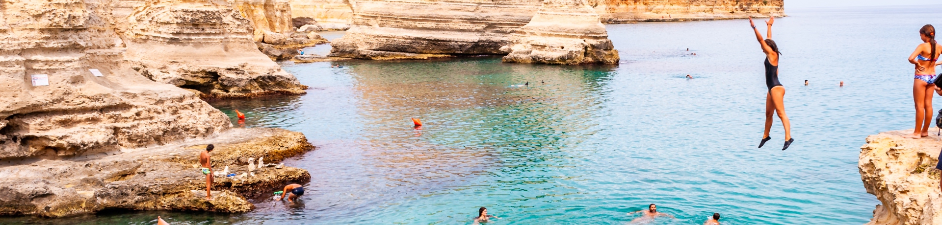 Spiaggia della puglia con bambini che si tuffano dalle scogliere