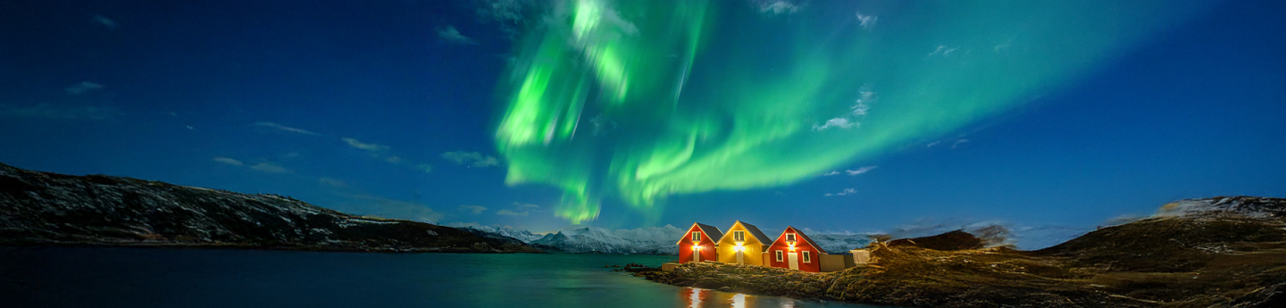 aurora boreale nel fiordo con casette illuminate di sera, Tromso, Norvegia