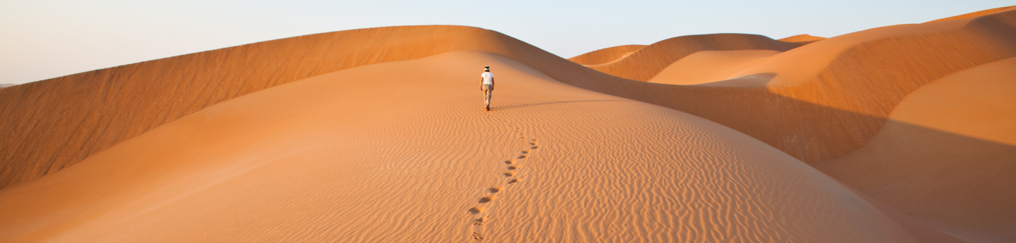 uomo che cammina tra le dune del deserto in Oman