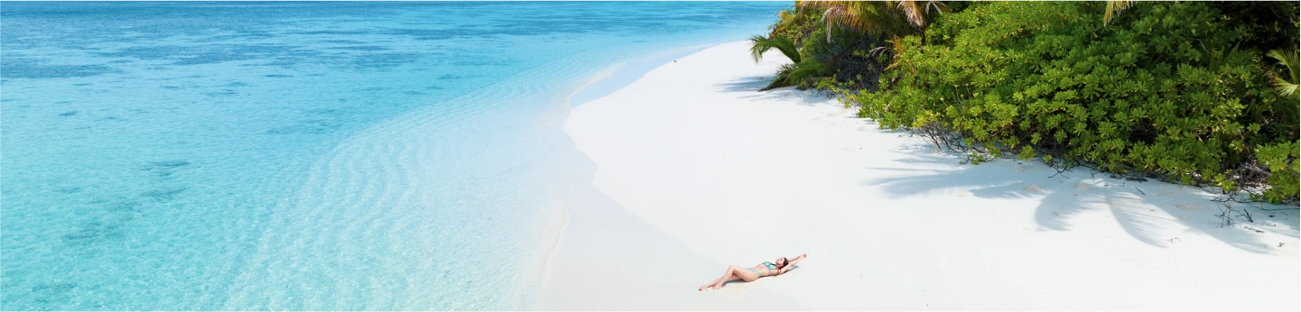 vista dall'alto di una ragazza che prende sole su una spiaggia di sabbia bianca e mare azzurro limpido alle Maldive